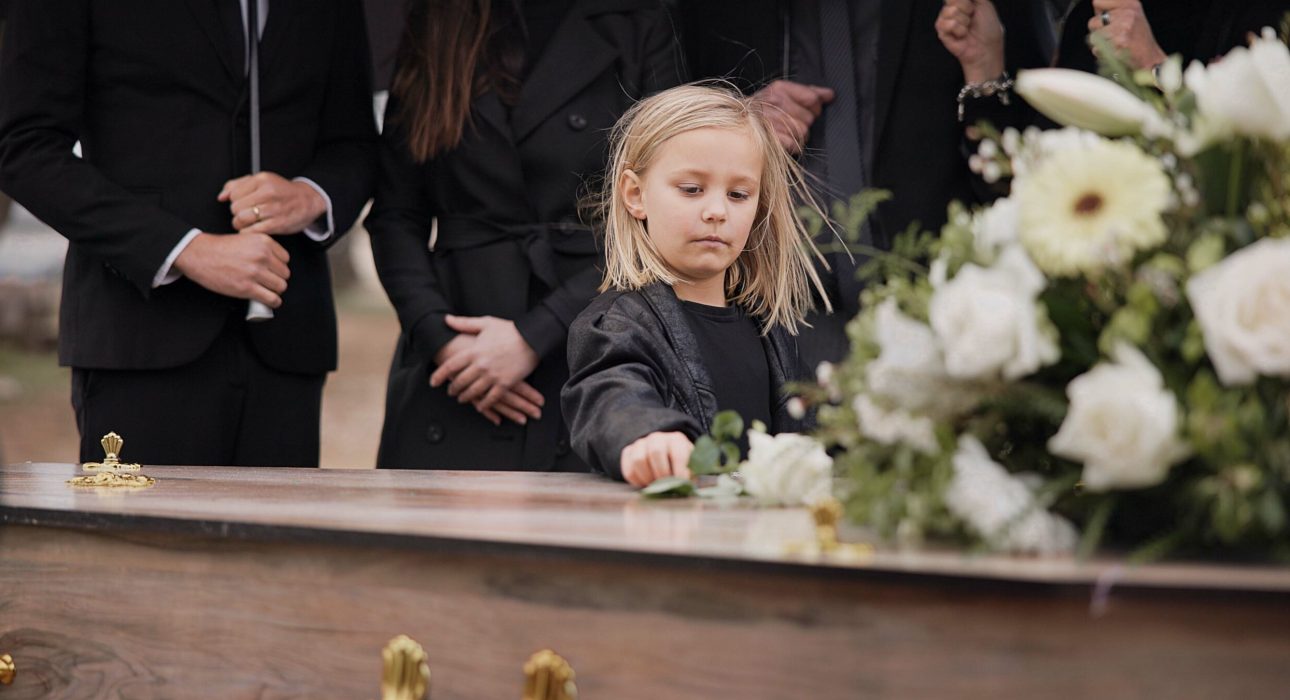 Death, grief and girl at funeral with flower on coffin, family and sad child at service in graveyar.